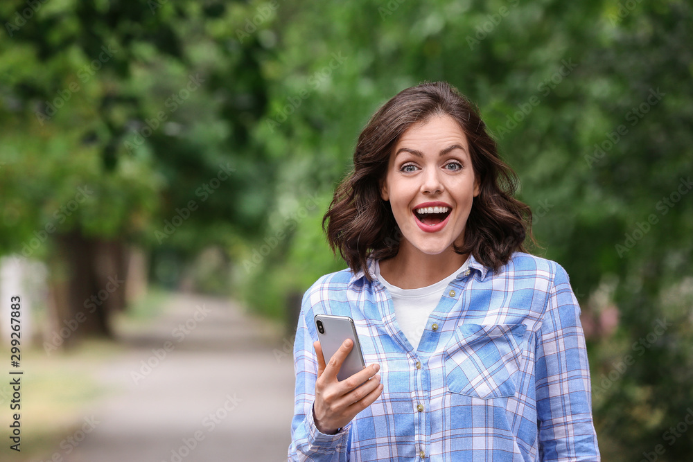 Surprised young woman with mobile phone outdoors