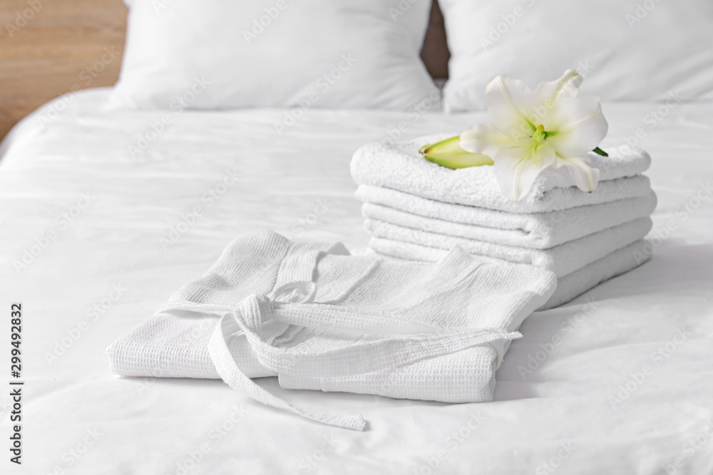 Soft clean bathrobe and towels on bed