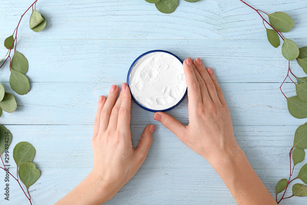 Hands of young woman and jar of cream on wooden background