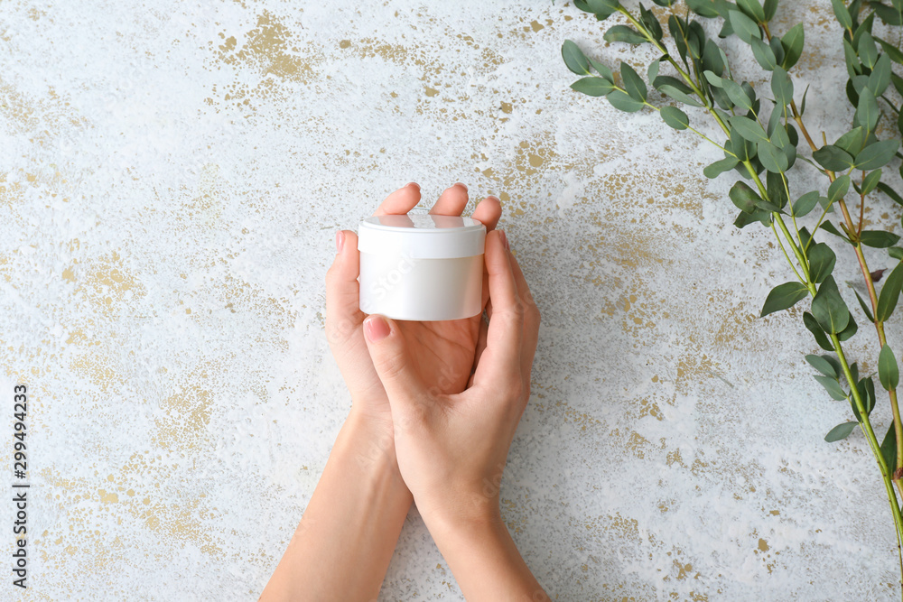 Female hands with jar of cream on light background