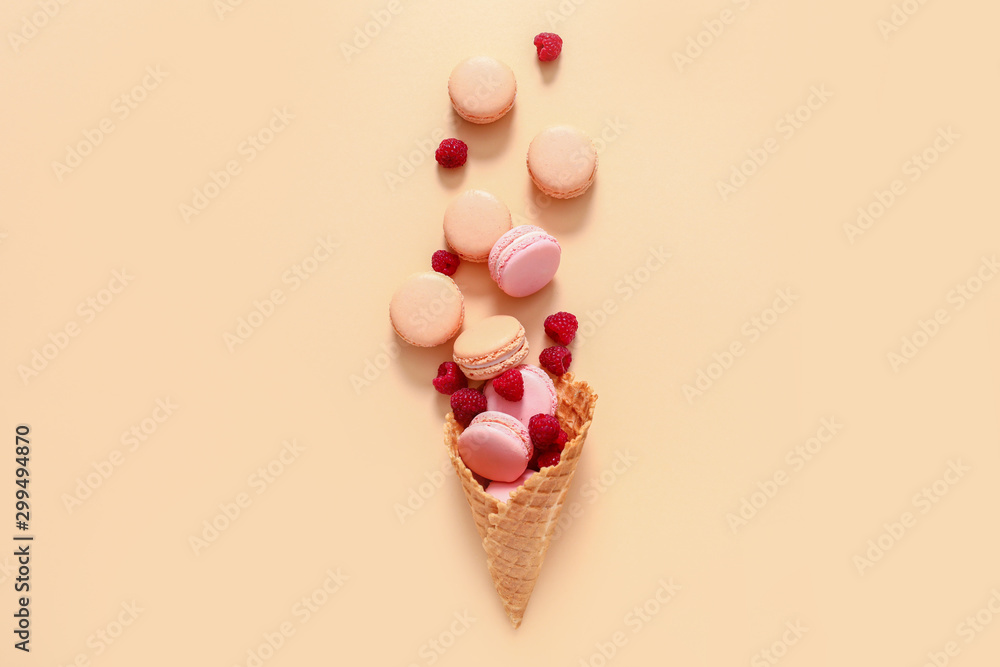 Wafer cone with tasty macarons and raspberry on color background