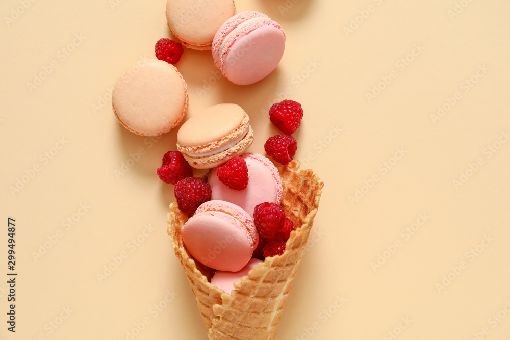 Wafer cone with tasty macarons and raspberry on color background