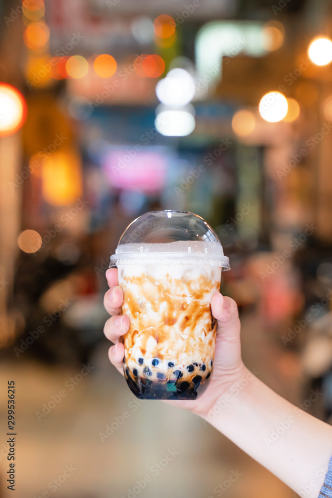 Young woman is holding, drinking brown sugar flavored tapioca pearl bubble milk tea with glass straw