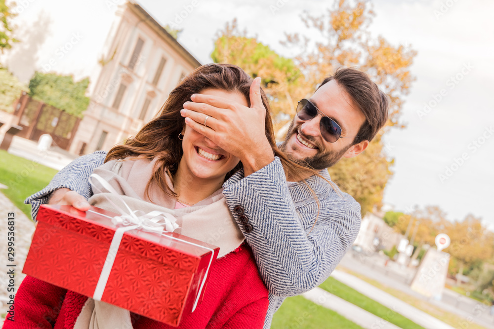 Smiling man surprises his girlfriend with present outdoor