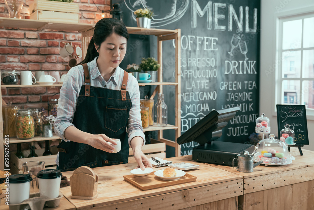 亚洲华裔女服务员把咖啡杯放在白色盘子和木托盘上。职业女性