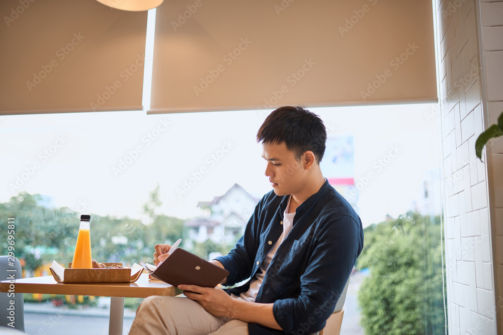 Businessman writing on notebook by cafe window, Concentrated on work, Side view of confident young m