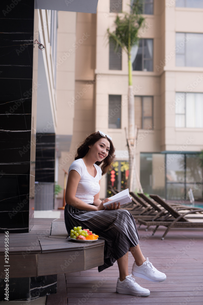 Pretty Asian woman reading book and enjoying fruit. Relaxation concept.