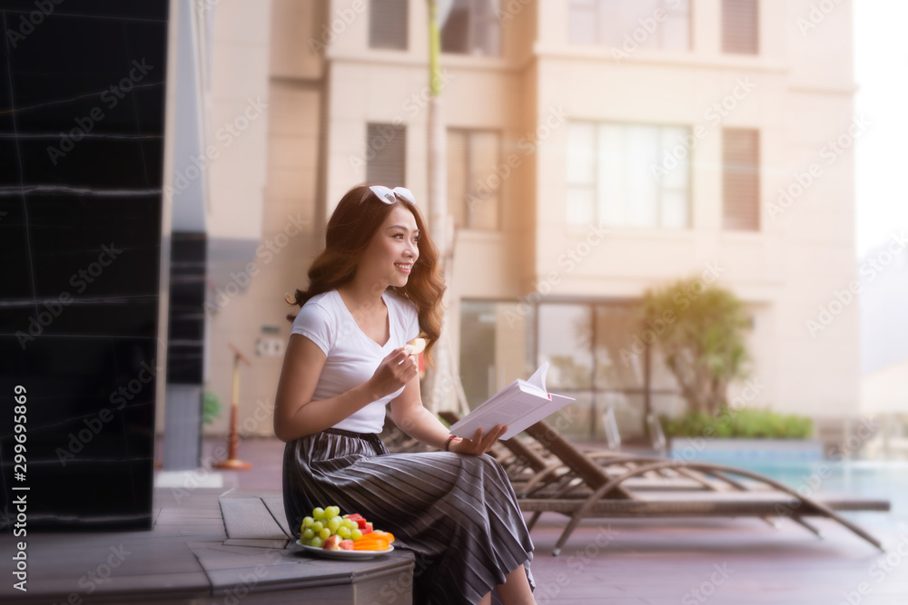 Woman in summer hat reading a book by the swimming pool. Vacation and relaxation, summer travel conc