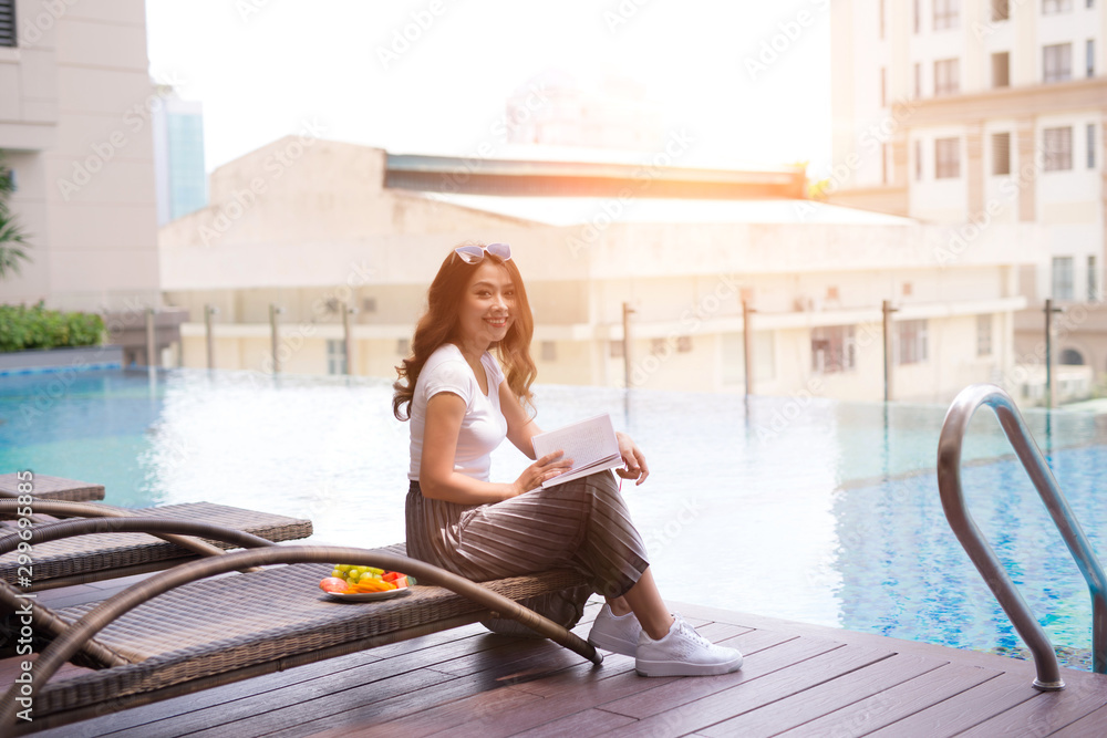 woman reading and relaxing near luxury swimming pool