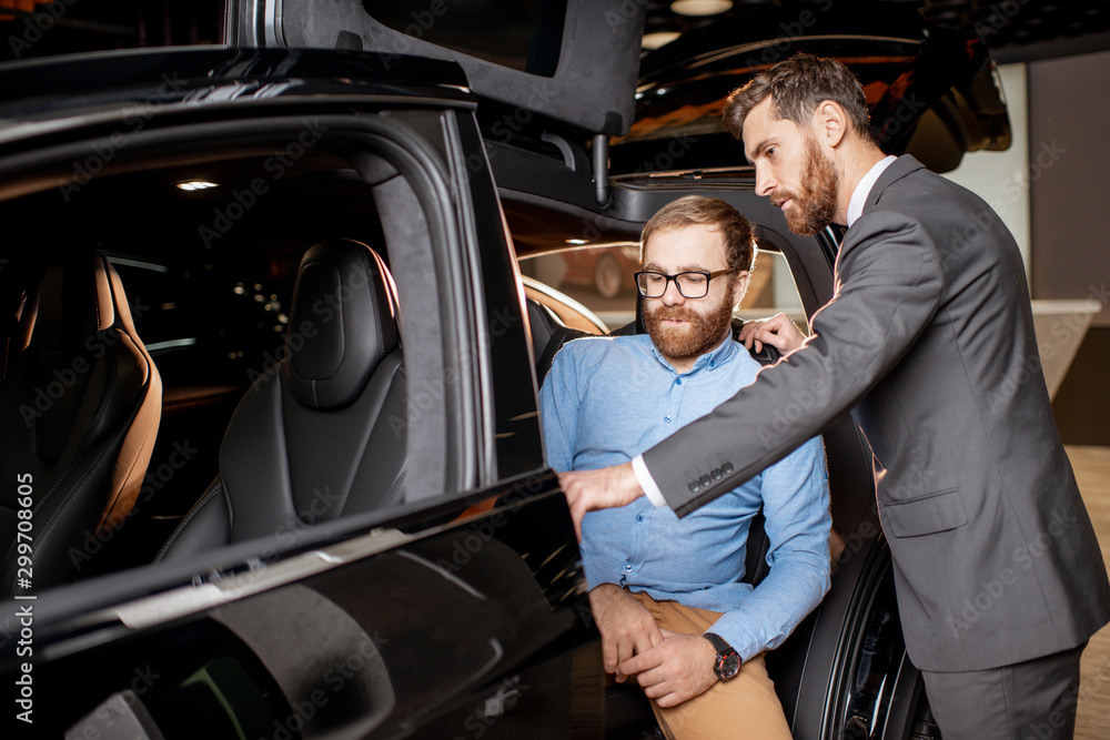 Customer with a sales manager inspecting modern car in the showroom