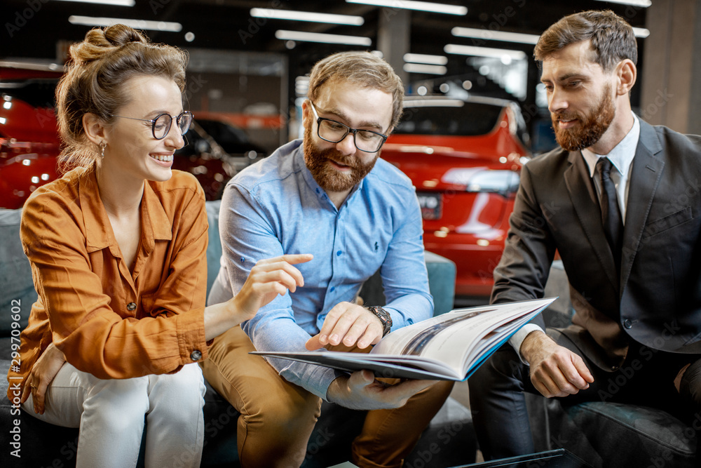 Couple with catalog and sales manager at the car dealership