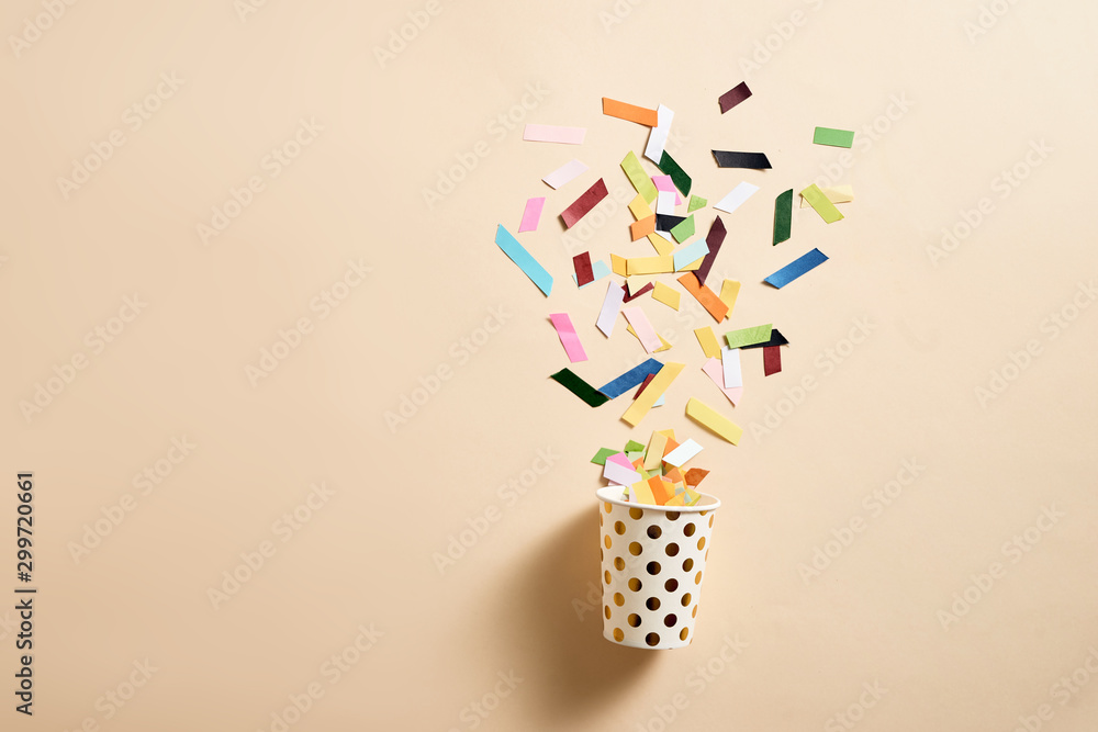 Drinking paper cup with multicolored confetti scattered on party background. Greeting card poster te