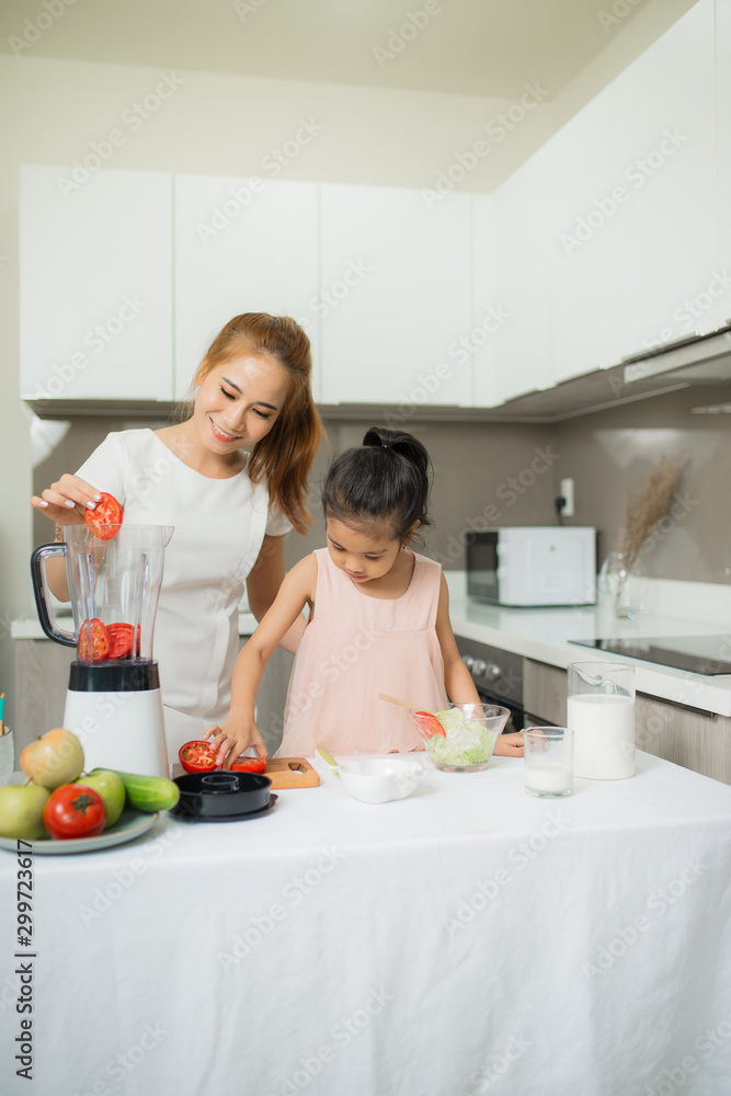 年轻的亚洲母亲和女儿正在制作新鲜挤压的番茄奶昔，女儿很开心