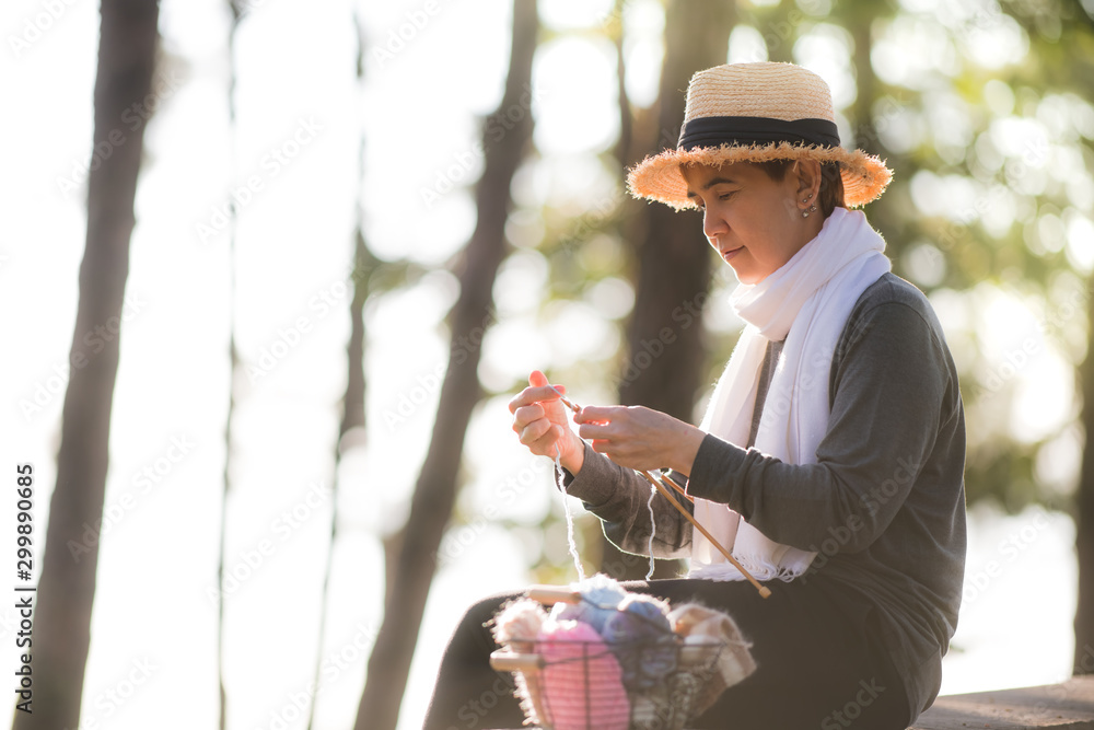 Middle aged Asian woman sitting on the bench and knitting for winter Christmas at beaitiful natural 