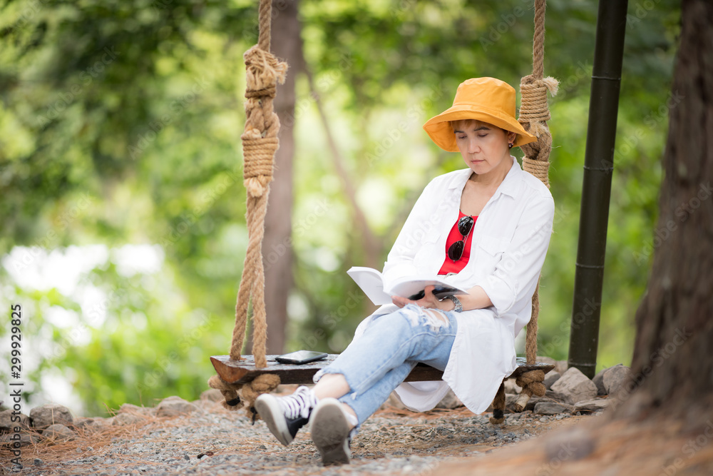 中年妇女坐在秋千上，在公园里看书