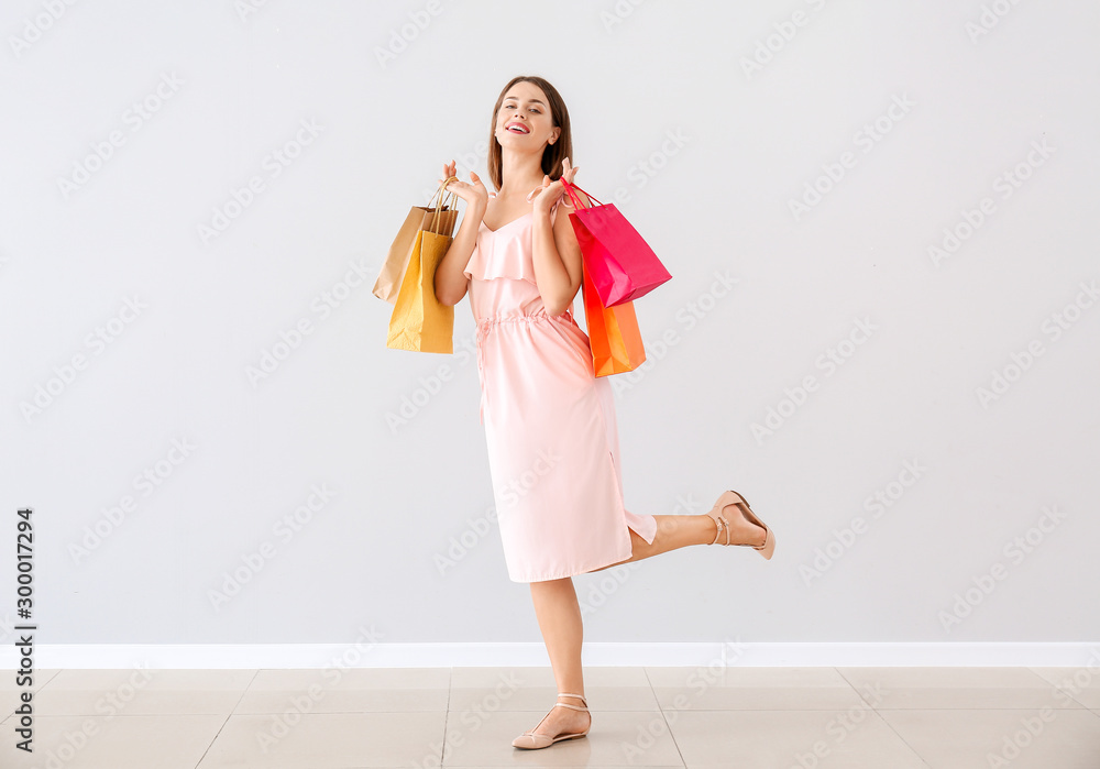 Beautiful young woman with shopping bags near light wall