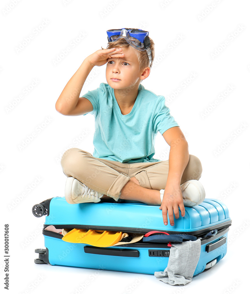 Cute little boy sitting on suitcase against white background