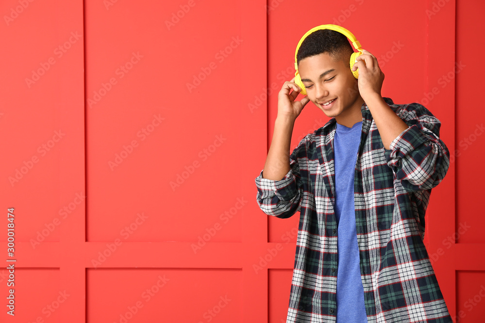 African-American teenage boy listening to music on color background