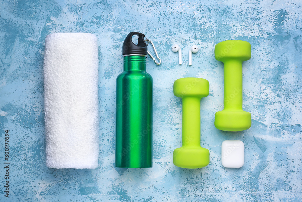 Sports water bottle, towel, earphones and dumbbells on color background