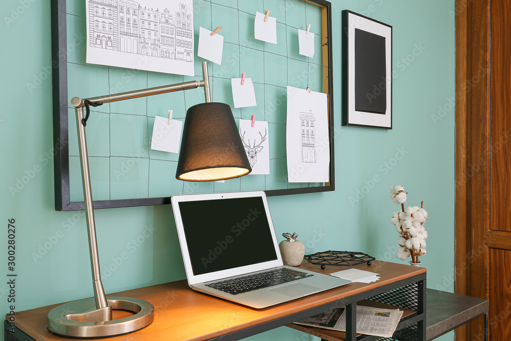 Comfortable workplace with mood board and laptop near color wall