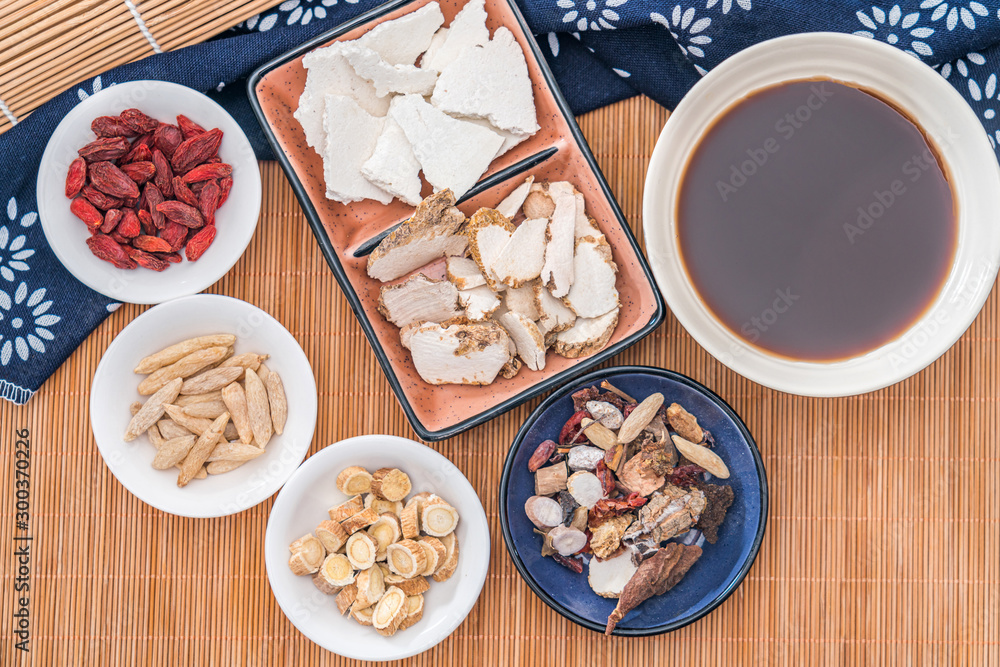 Various Chinese herbal medicines and a bowl of Chinese herbal medicine soup scattered on bamboo mats