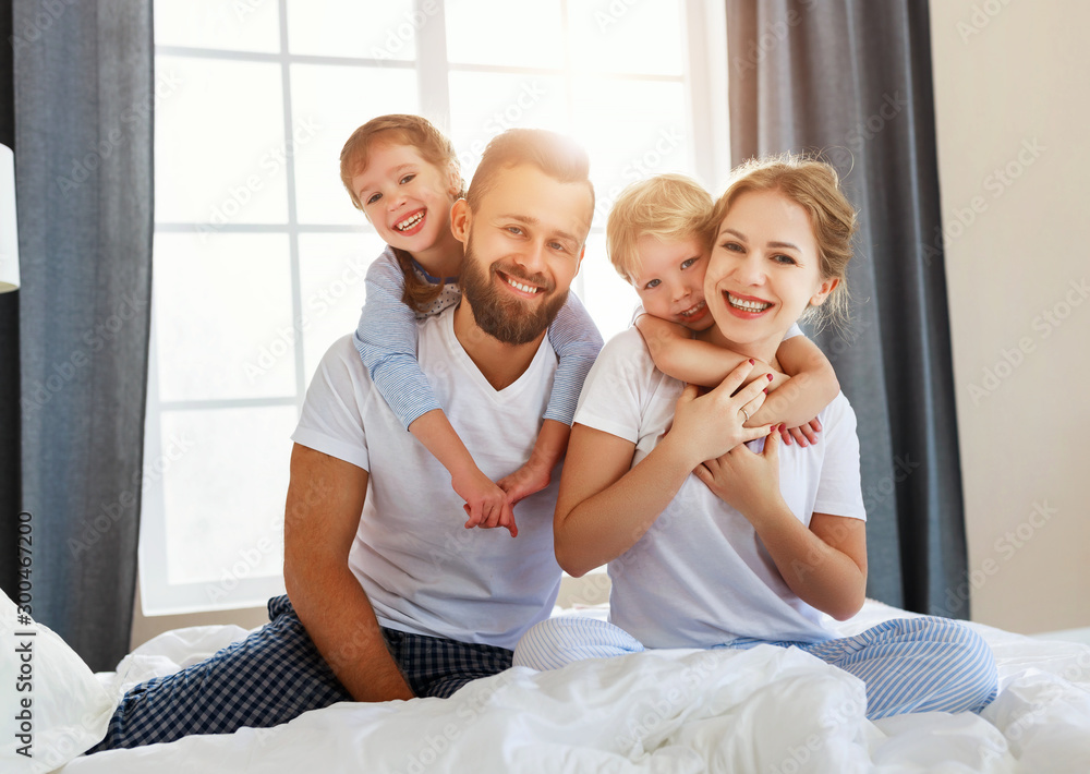 happy family mother, father and children laughing, playing and smiling in bed   at home