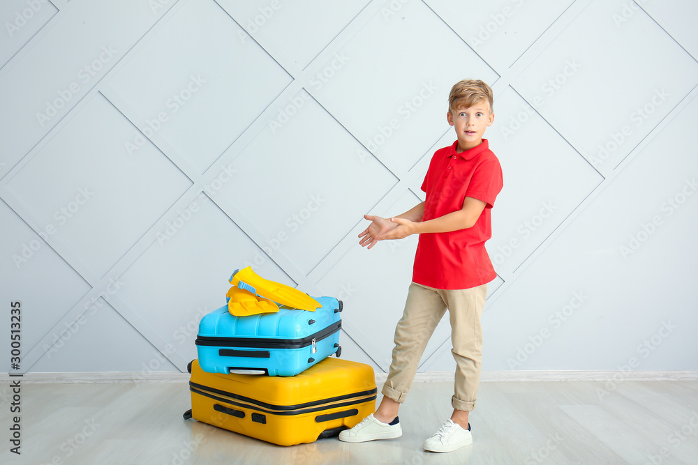 Surprised little boy with luggage near light wall