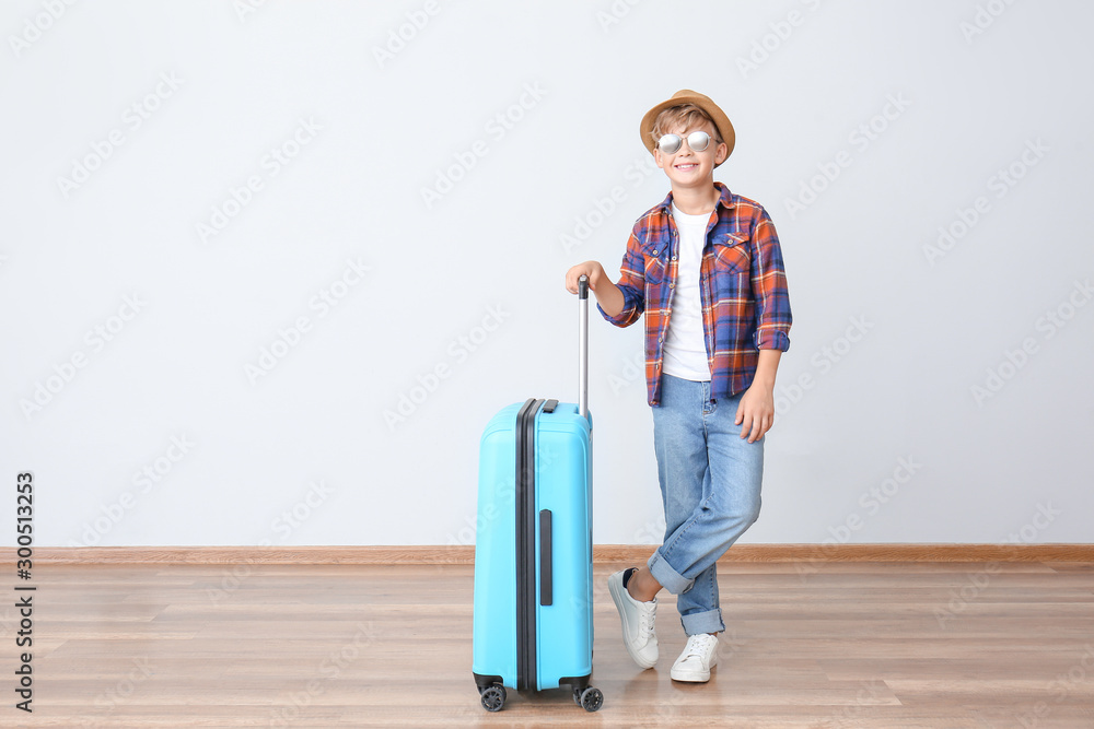 Cute little boy with suitcase near light wall