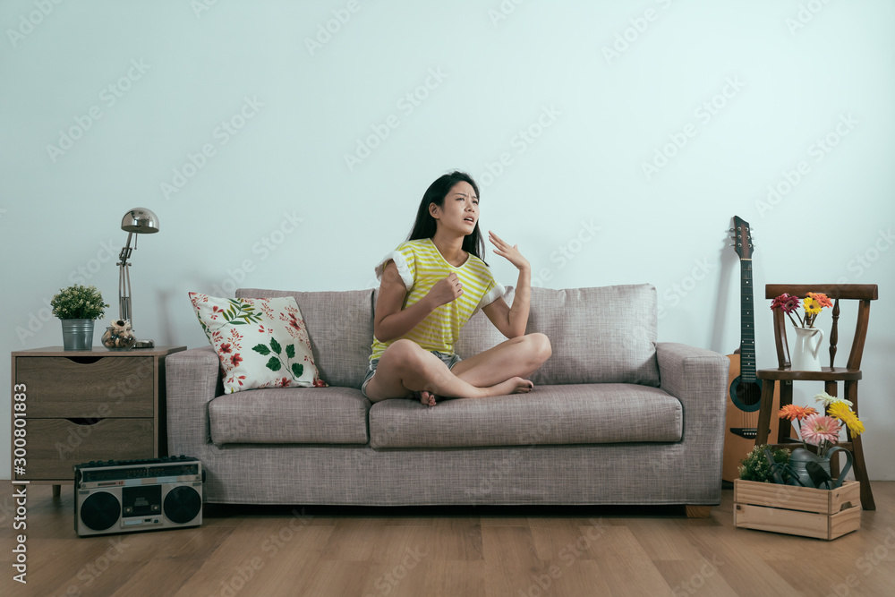 年轻的亚洲裔日本女性在夏天穿着衣服，独自坐在客厅舒适的沙发上为自己降温