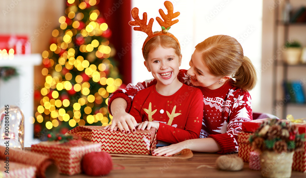 happy family mother and child pack Christmas gifts at home near Christmas tree