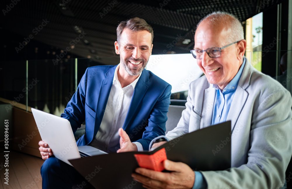 Younger and older businessman talking about documents during meeting in modern business lounge