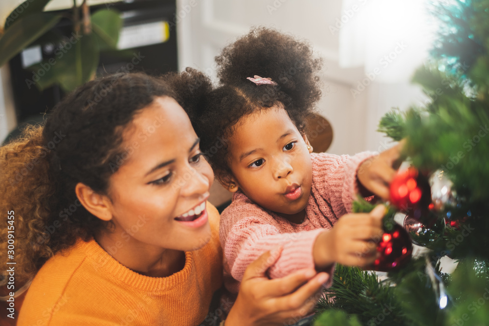 Black african mother and her cute daughter decorating christmas tree for christmas and happy new con