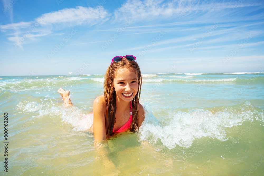 Happy girl lay in the sea waves smiling on a beach