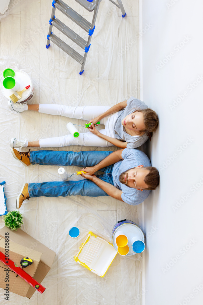 young tired couple is repairing and painting   wall at home.