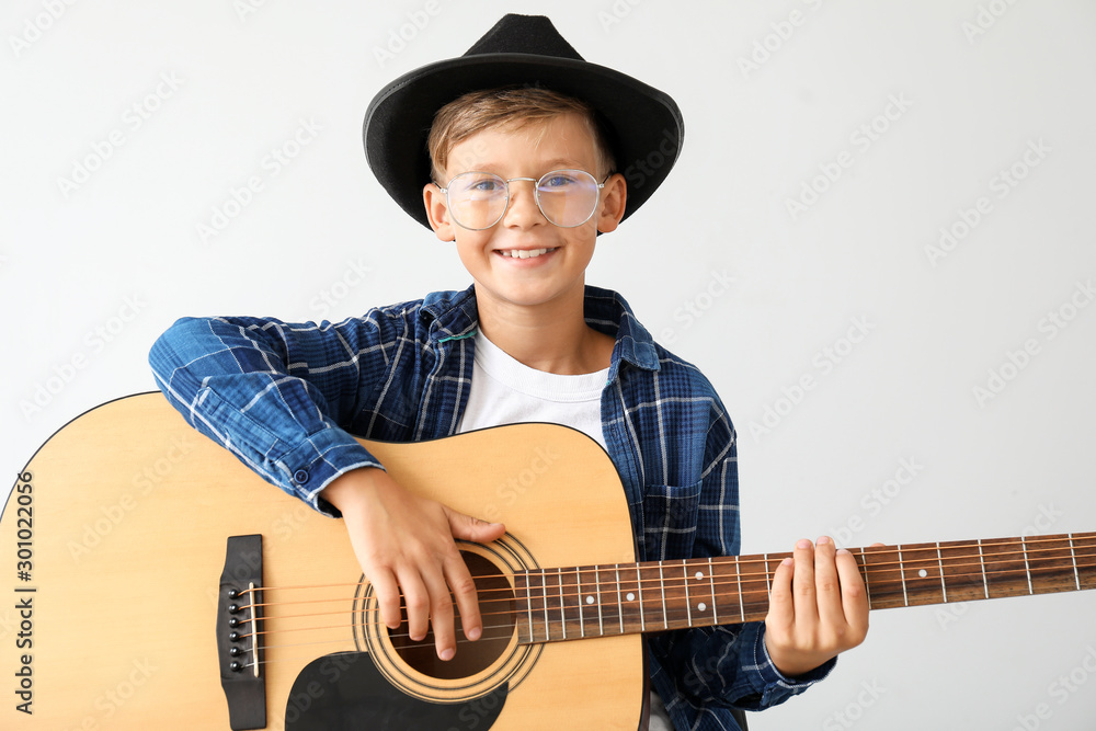 Little boy playing guitar on light background