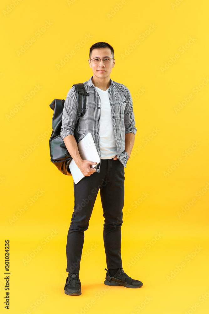 Male Asian student with laptop on color background