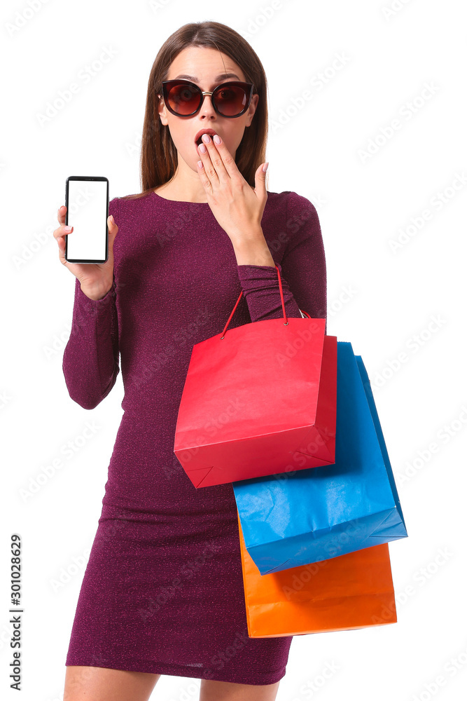 Surprised young woman with shopping bags and mobile phone on white background