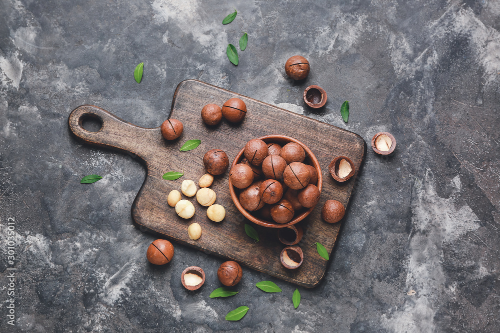 Bowl with tasty macadamia nuts on dark background