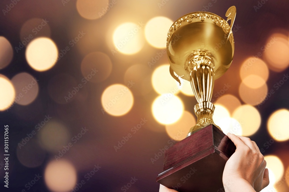 Hands holding golden trophy on light background