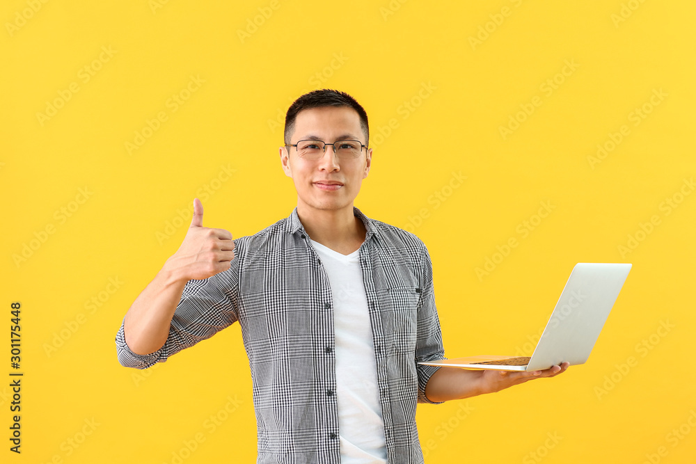 Male Asian programmer with laptop showing thumb-up on color background