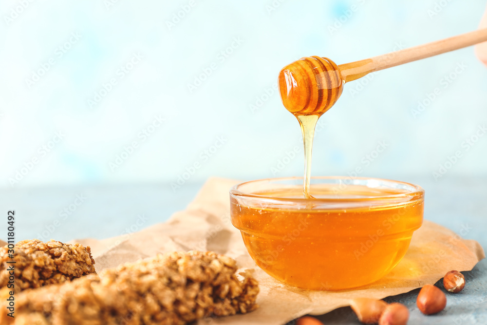 Bowl with tasty honey, spoon and granola on color background