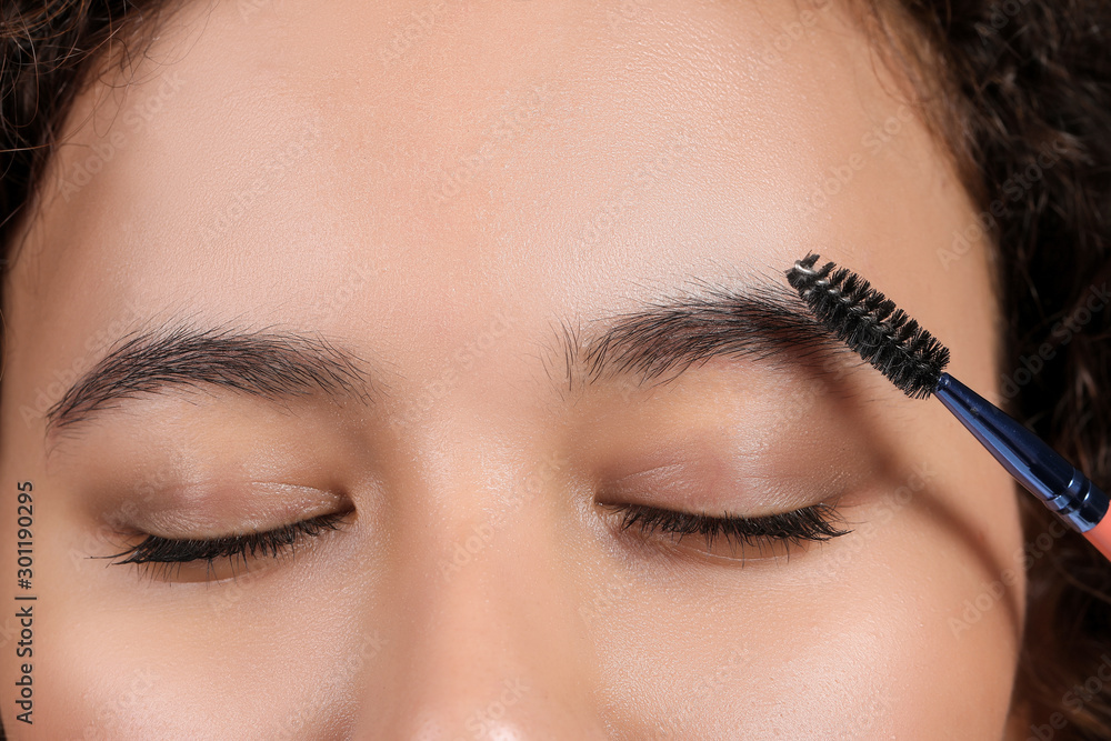 Young woman correcting shape of her eyebrows, closeup