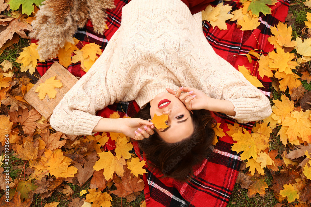 Stylish young woman lying on plaid on autumn day, top view