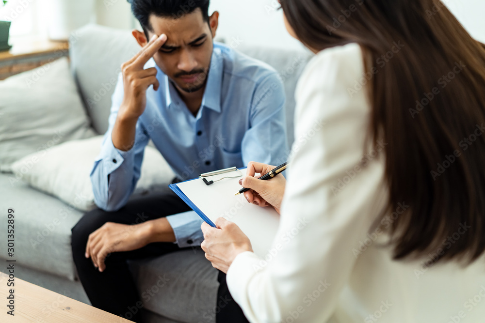 Young male patient sitting on sofa explaining and consulting his problem with sad face to profession