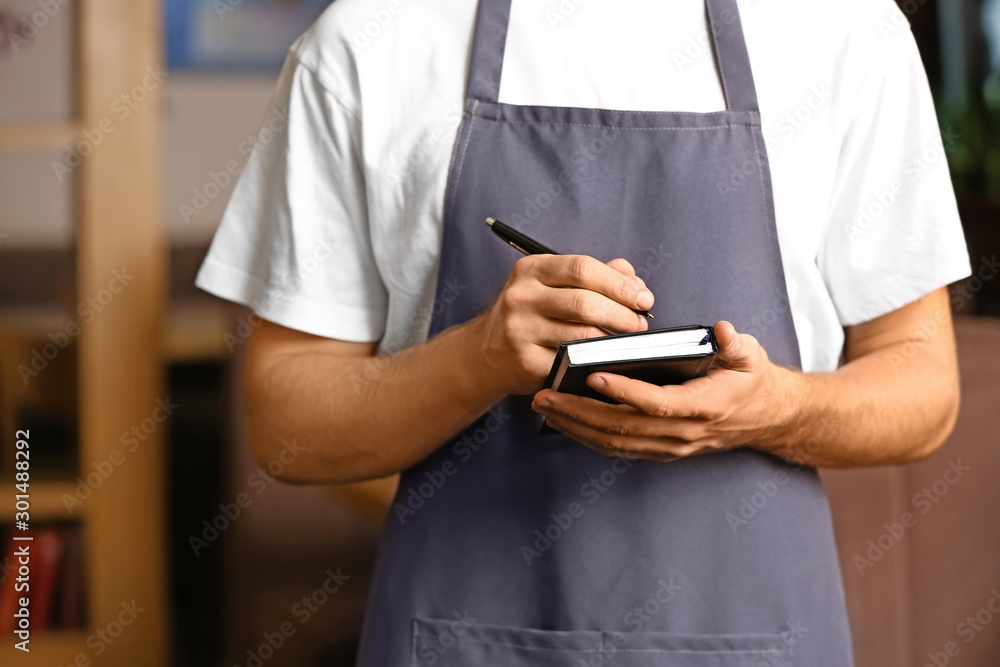 Young male waiter with notebook in restaurant, closeup