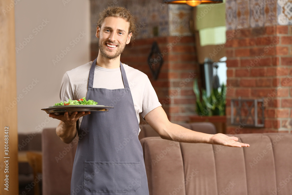 Young male waiter inviting somebody in restaurant