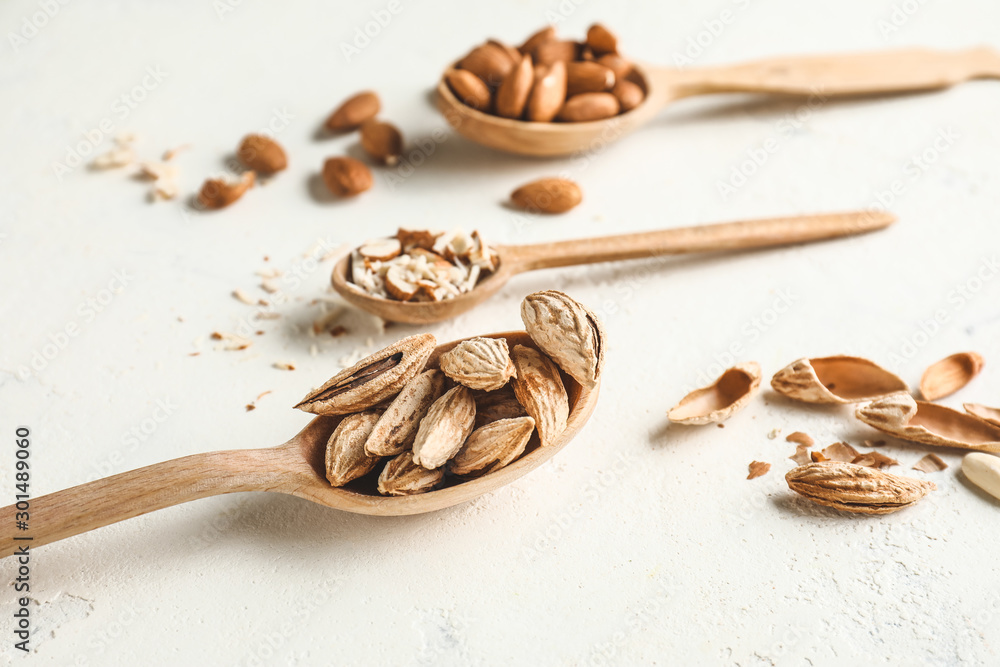 Spoons with tasty almonds on white background