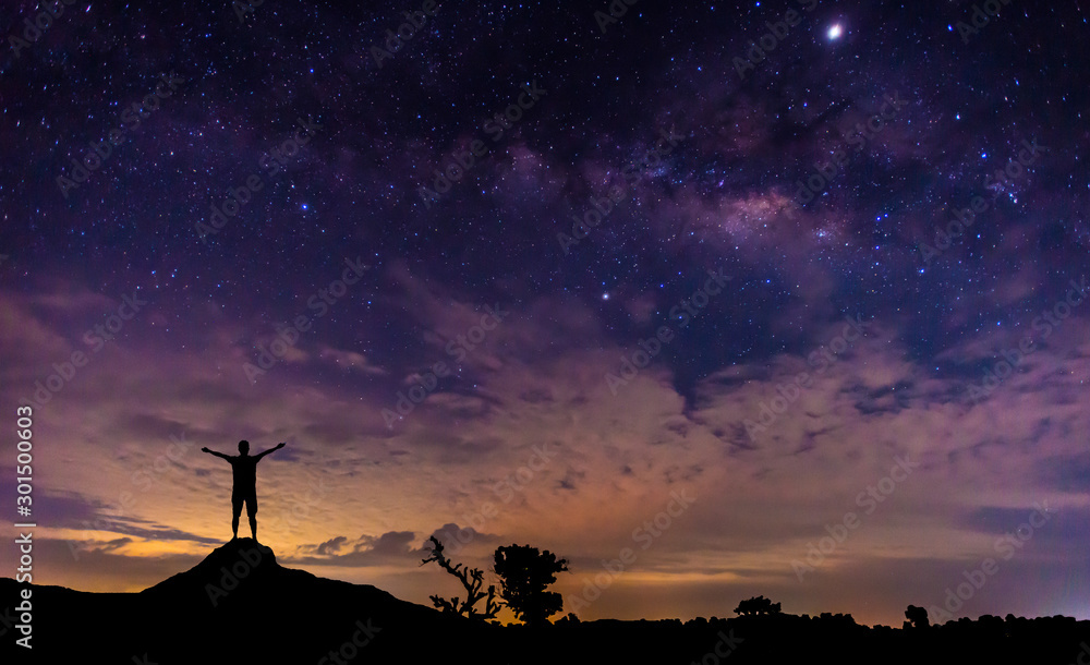 旅行者的剪影站在山顶。全景蓝色夜空乳白色，星星在黑暗的背面。