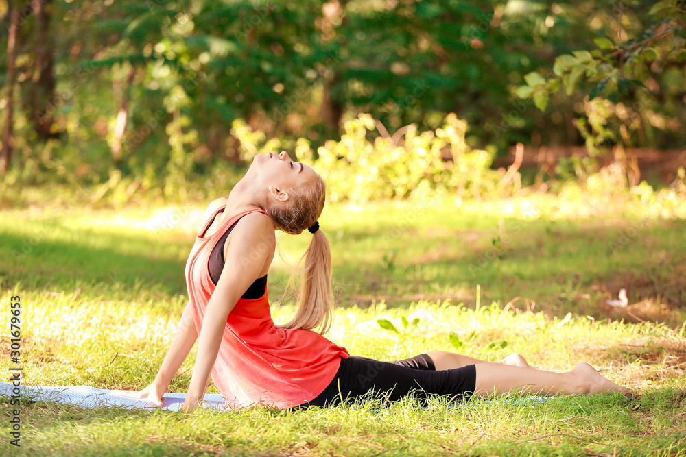 Beautiful young woman practicing yoga in park