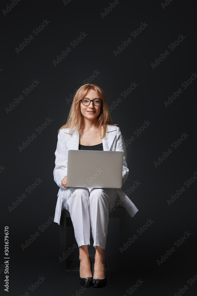 Stylish mature businesswoman with laptop on dark background